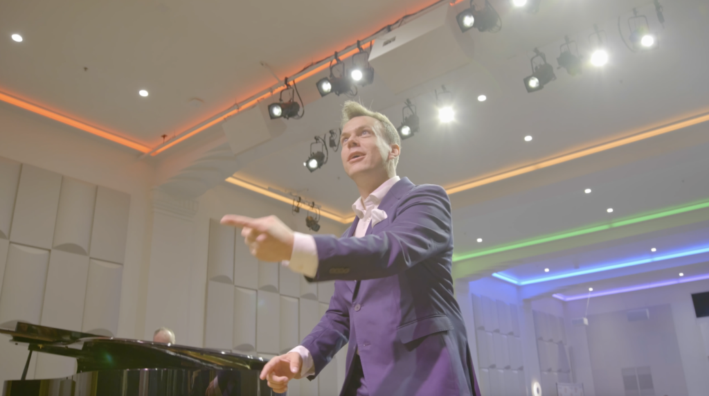 Jacob Stensberg conducts looking upwards on stage at The Chan National Queer Arts Center.