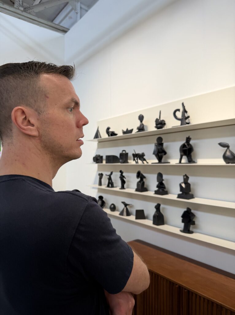 • Jake Stensberg standing in profile, looking at shelves displaying small black sculptures